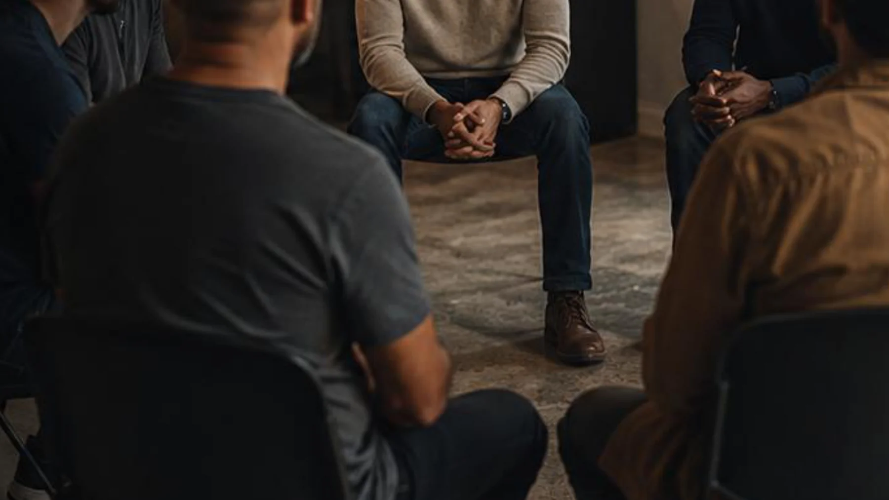 Homens sentados em roda de conversa, em uma imagem escura e acolhedora.